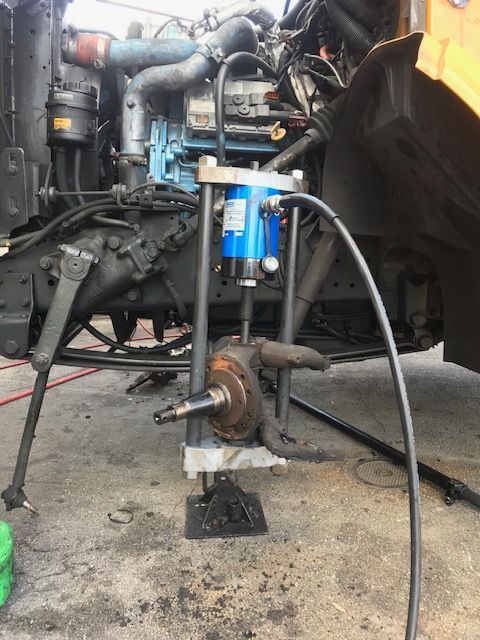 Hydraulic press removing a wheel hub from a truck. The truck is orange and black.