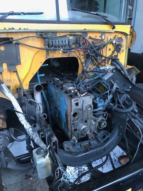 Engine block partially installed in a yellow vehicle's engine bay, with exposed wiring and components.