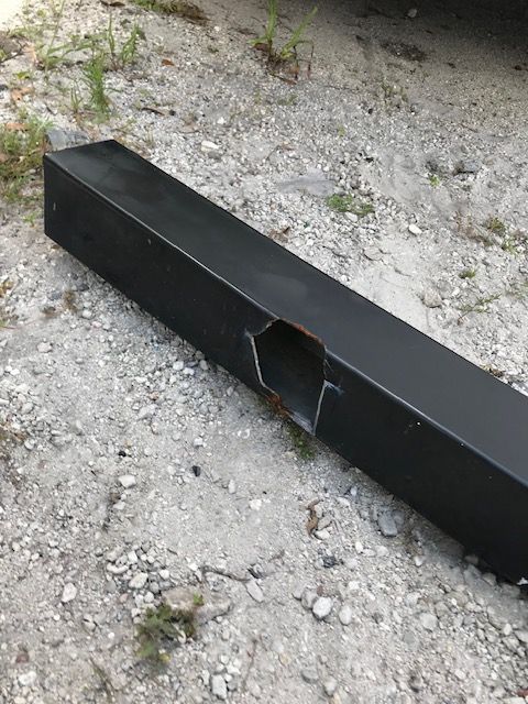 Black metal beam on gravel ground, with a large, hexagonal cut.