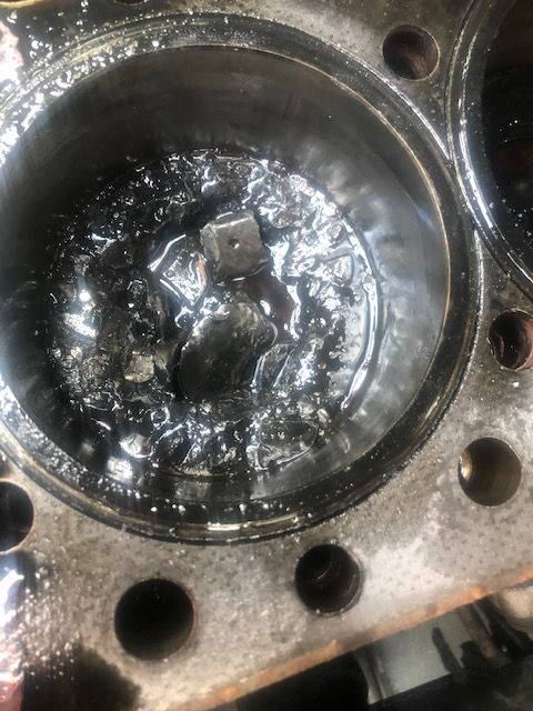 Cylinder in an engine block filled with black residue and a small metal piece.