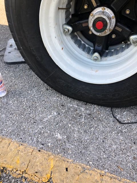 Black car wheel with white rim on asphalt, yellow curb in the foreground.
