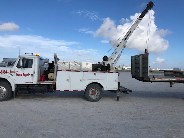 White tow truck lifting a flatbed trailer under a blue sky. 