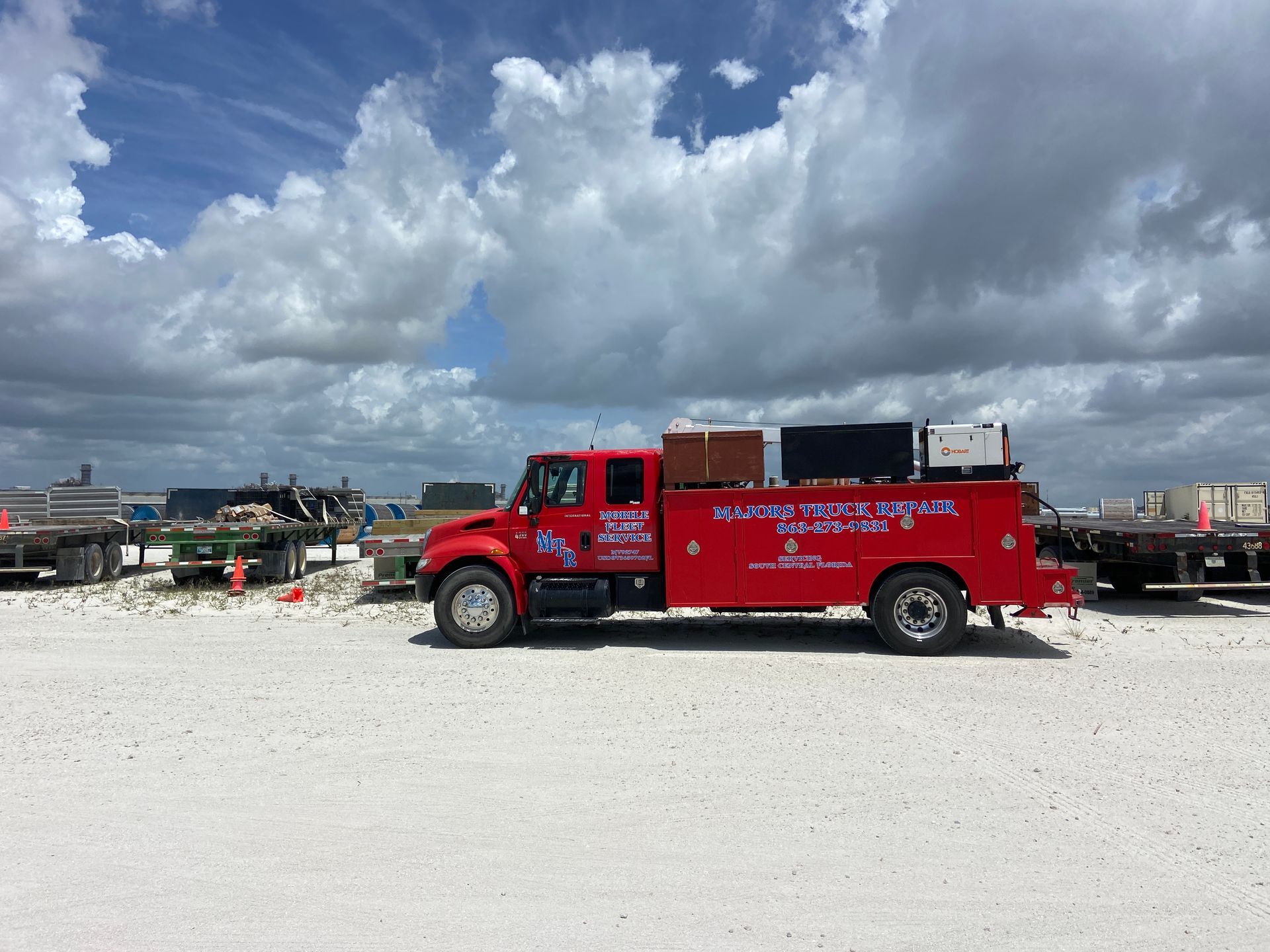 Red work truck with equipment on a construction site under a cloudy sky.