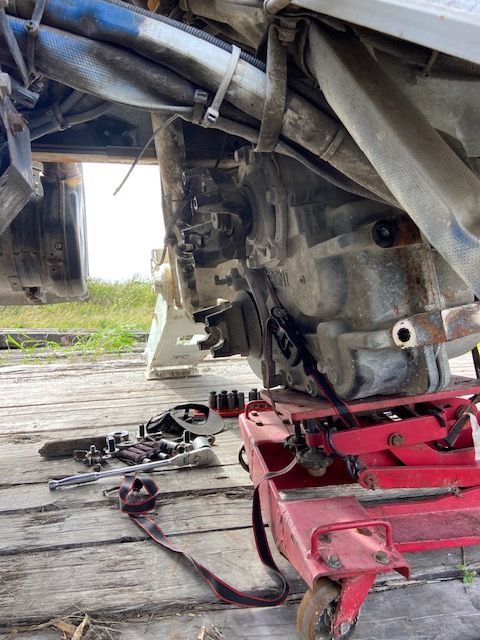 A vehicle's rear axle is being worked on with tools scattered nearby; it's resting on a red jack.