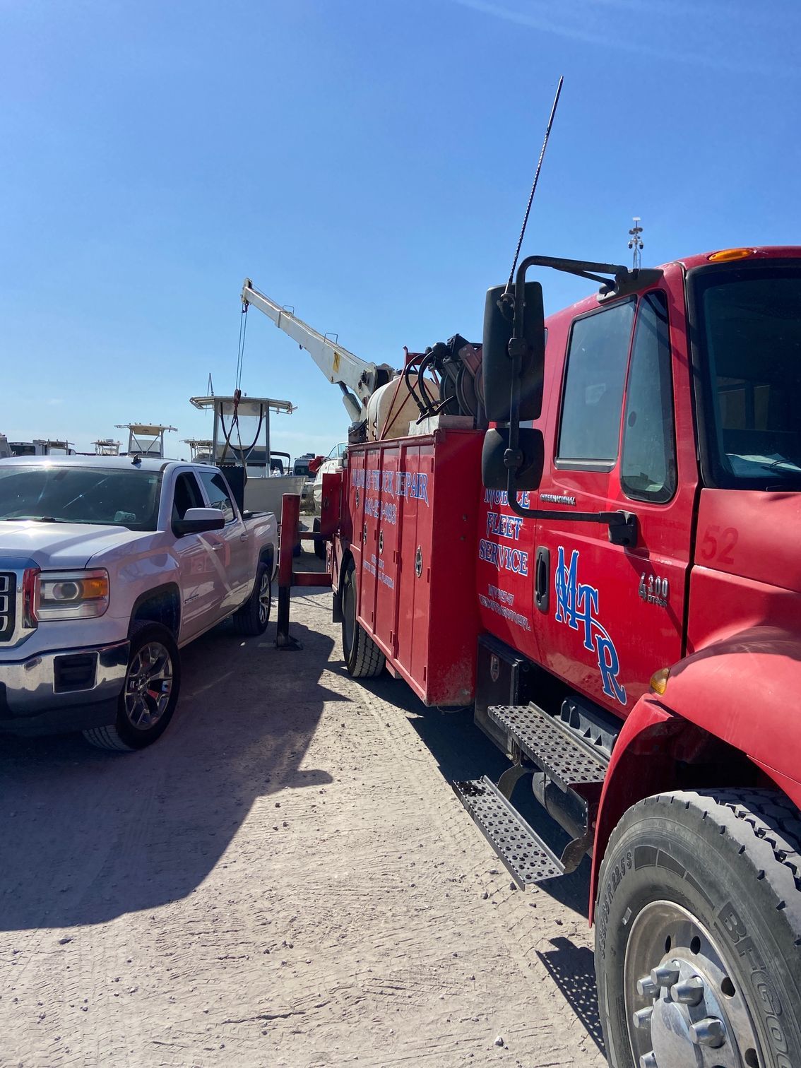 A red tow truck lifting a boat, parked next to a white pickup truck, on a sunny day.