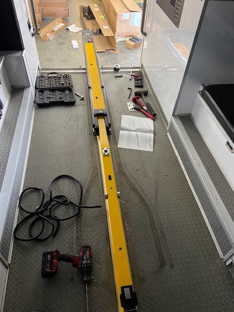 Interior view of a vehicle under repair. Yellow safety bar laid out on the floor with tools and instructions nearby.
