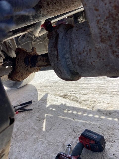 Rusting vehicle exhaust pipe components under a car, wrench and tool visible.