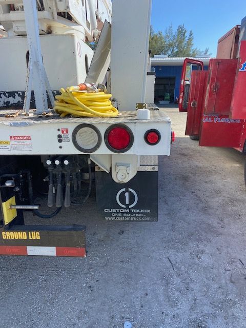 Back of a white truck with taillights. Yellow cable on the bed.  Black mud flap with logo.