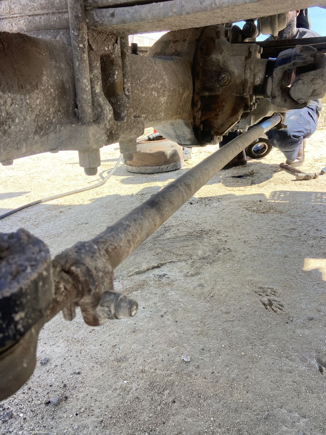 Rusty truck axle and steering linkage. Mechanic working on the vehicle outdoors.