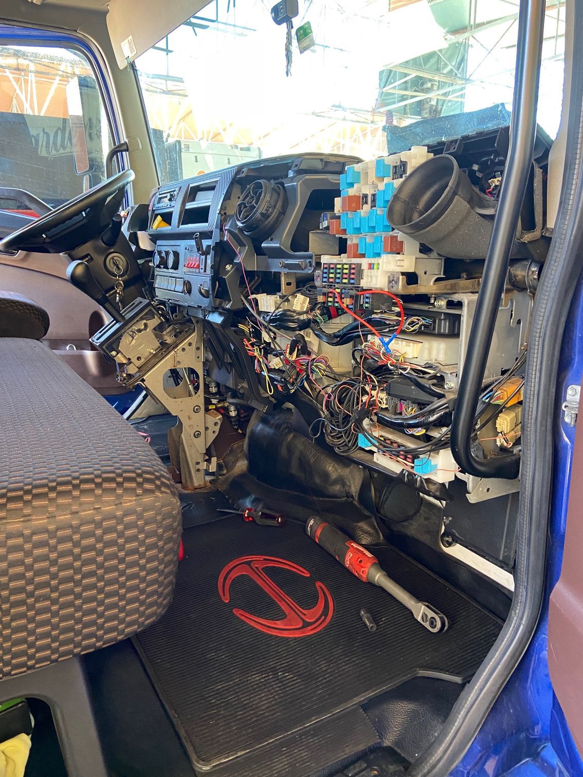 Interior of a truck with dashboard disassembled, revealing wires and components. Tools on the floor, Hino logo visible.