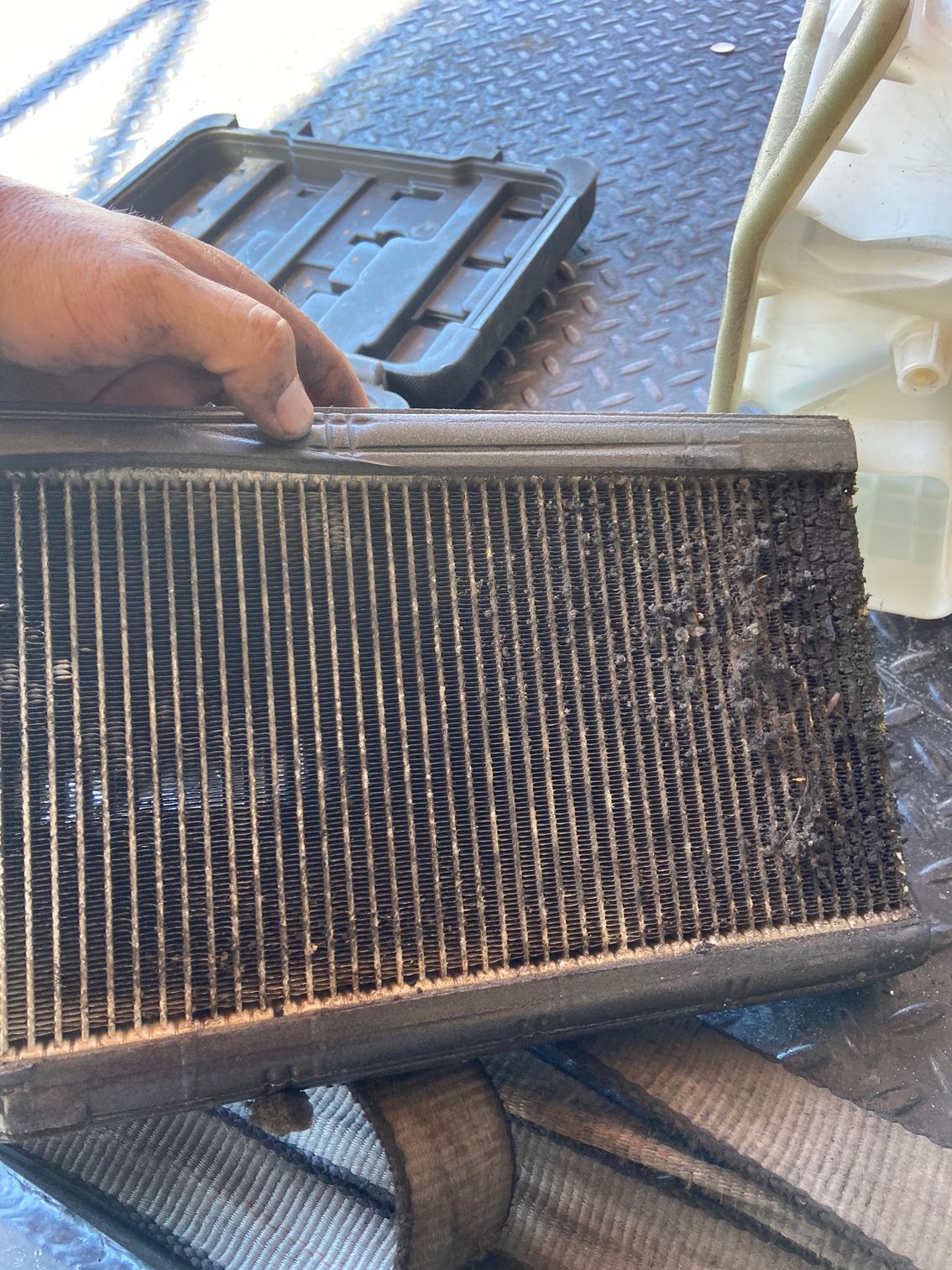 A person holding a car air conditioning evaporator core; showing debris and corrosion.