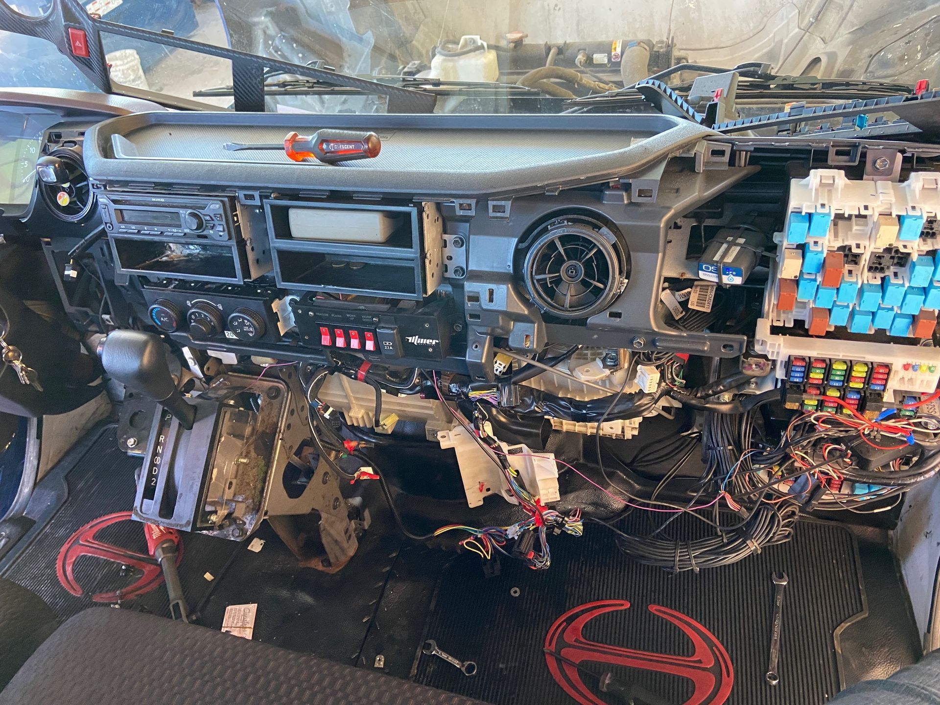 Dashboard of a vehicle disassembled, wires exposed, tools visible.
