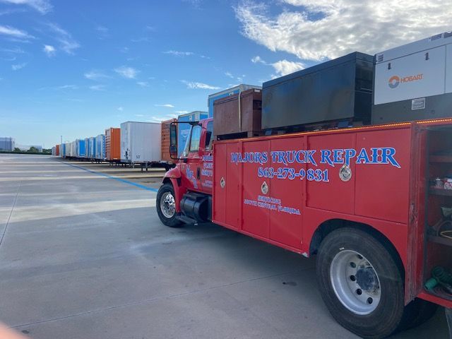 Red repair truck parked next to a row of trailers. Truck has tools and logo 