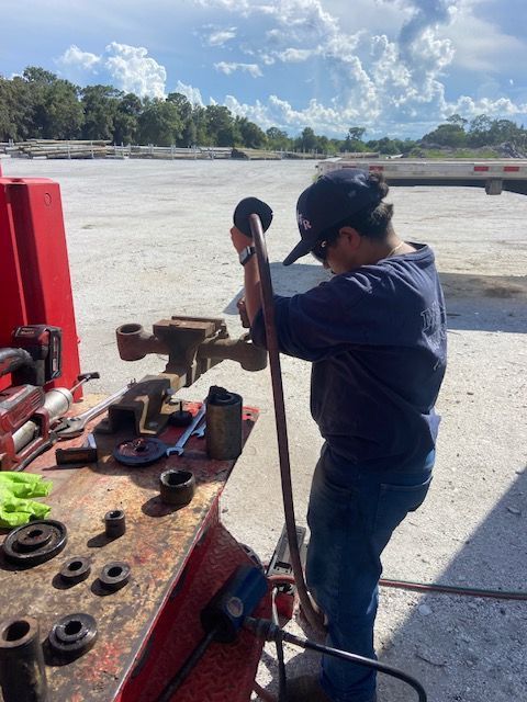 Person working on machinery at an outdoor worksite, using a wrench.