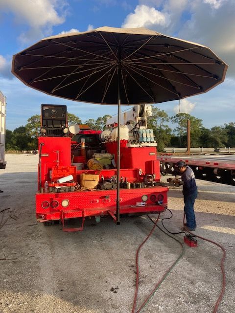 Red work truck with large umbrella; worker near it.