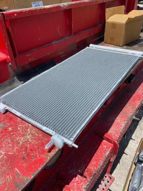 New car AC condenser, silver, on a red truck bed, with a cardboard box in the background.