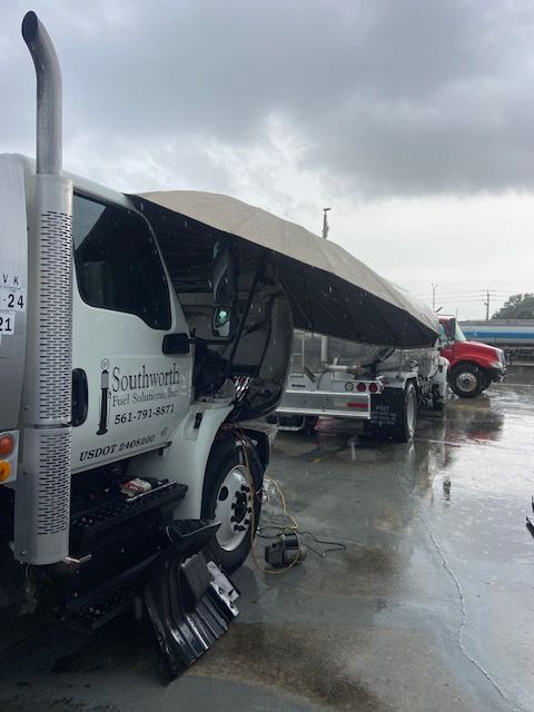 A white truck with a tilted trailer in a rainy environment. The truck has the company name 