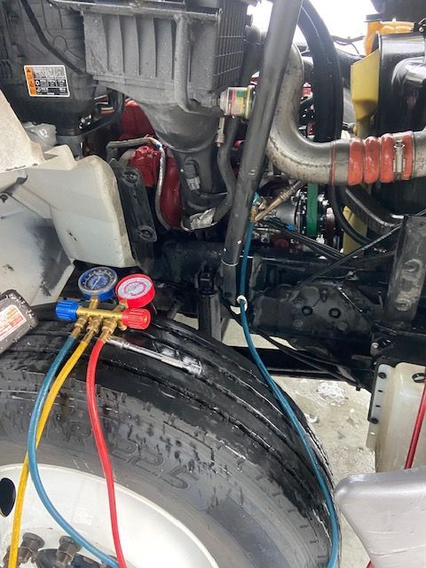 A semi-truck engine bay with air conditioning gauges attached for testing.