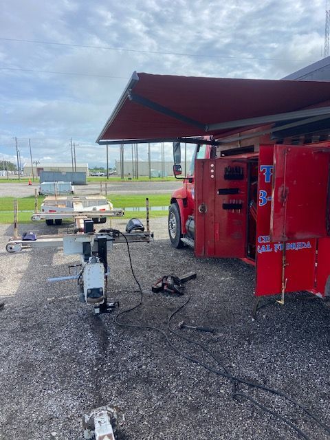 Red truck with open doors under a red awning, parked outdoors, with tools scattered nearby.