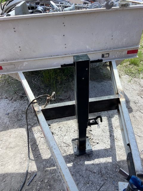 Aluminum boat trailer with a black jack, parked outdoors.
