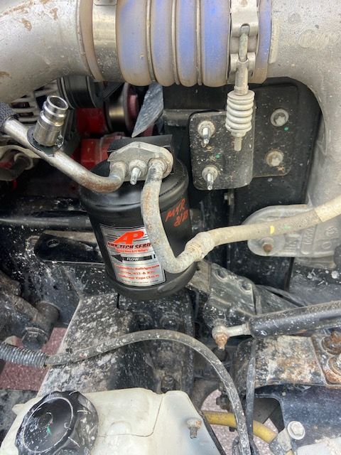 Engine compartment showing a black air dryer with connected hoses and a metal bracket.