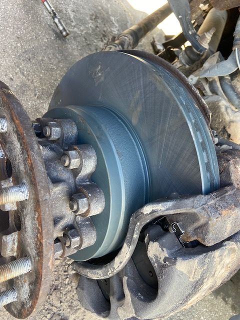 New brake rotor installed on a vehicle's front wheel. Gray disc and silver bolts are visible.