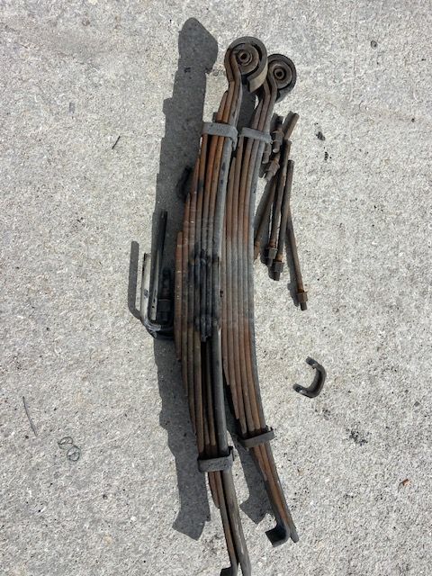Rusty leaf springs and hardware on a concrete surface, suggesting automotive repair or parts.