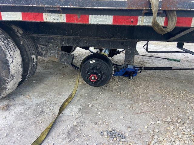 Trailer tire being changed with a jack on a concrete surface.