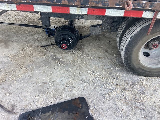 Truck trailer axle with tire, red wheel studs, and black brake components on a concrete surface.