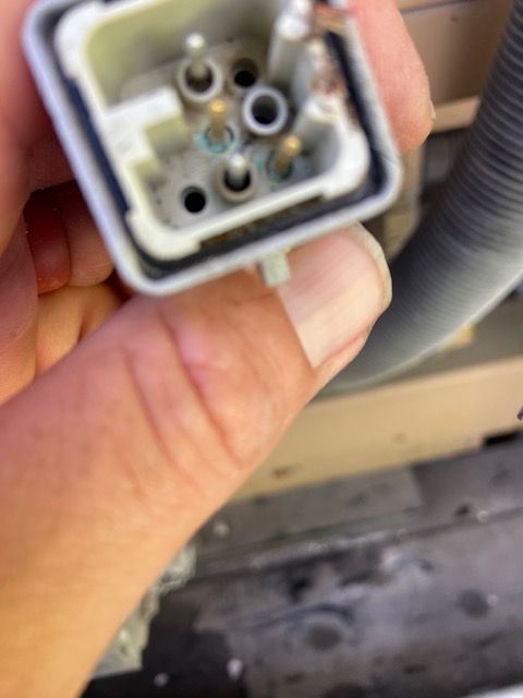 Close-up of a hand holding a light grey electrical connector with several pins and holes.