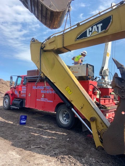 A red truck with a yellow excavator arm being serviced by a construction worker.