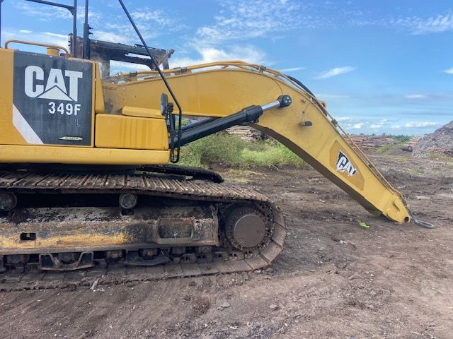 Yellow Caterpillar 349F excavator with tracks on muddy ground, under a cloudy sky.