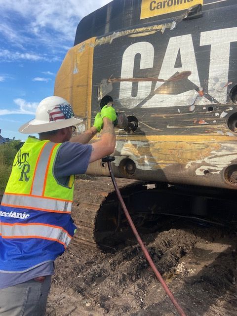 Person in safety vest working on a CAT excavator outdoors.
