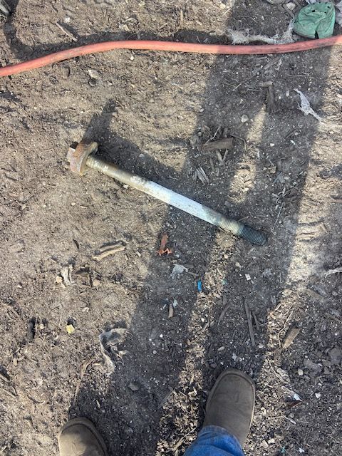 A large, rusty bolt on the ground next to a person's boots. An orange hose lies above the bolt.