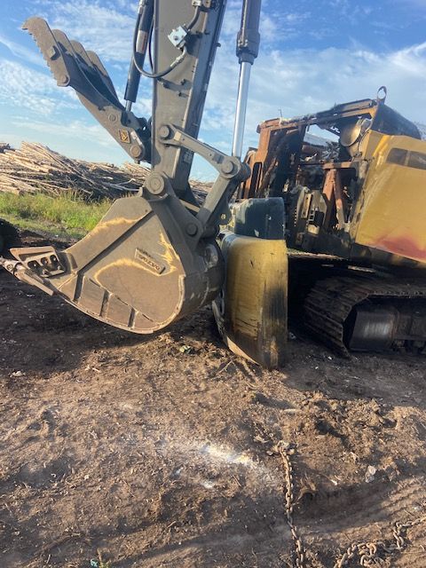 Excavator with a large bucket digging into dirt. Yellow paint, set outdoors in daylight.