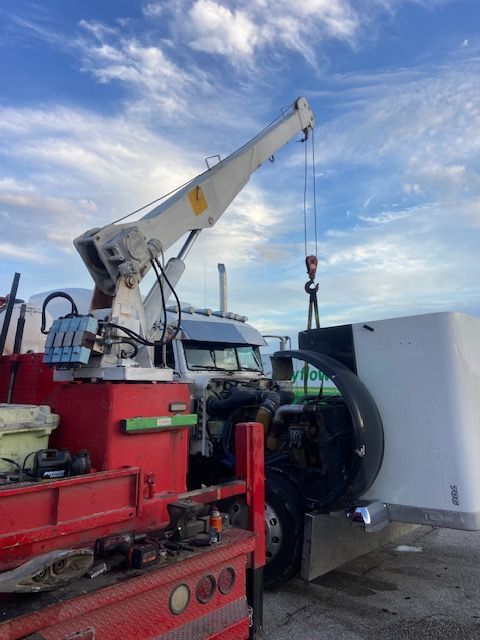 A crane lifting a large white box near a truck with red elements against a blue sky.