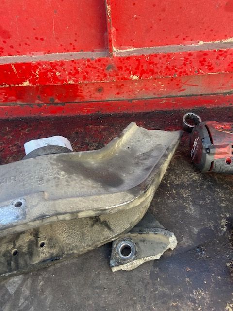 Damaged metal car part with a detached piece, likely from a vehicle's undercarriage, on a red surface.