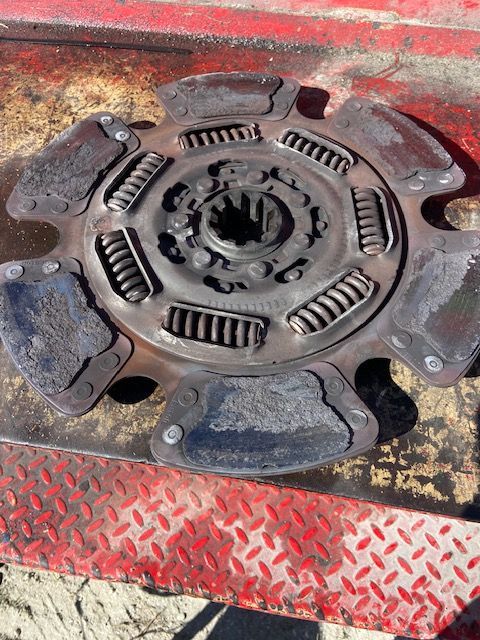 Worn, circular clutch disc with springs and worn friction pads on a red surface.