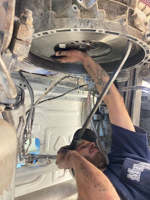 Mechanic working on a truck engine. He is lying under the vehicle, with arms reaching toward the flywheel.
