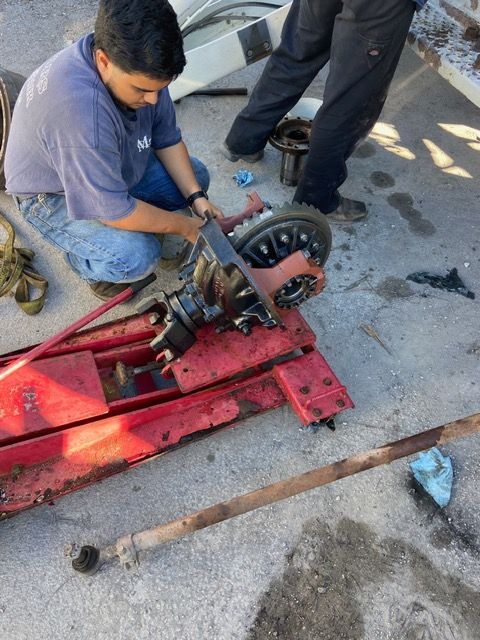 Two people repairing a differential on a red lift. One man is tightening something; another man stands nearby.