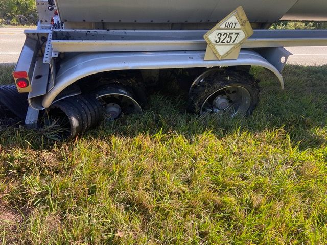 Trailer with a tank off-road in grass, showing the wheels and a 3257 DOT hazard sign.