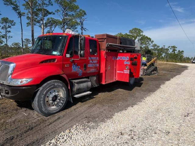 A bright red service truck is parked on a dirt shoulder next to a gravel road under a clear blue sky.