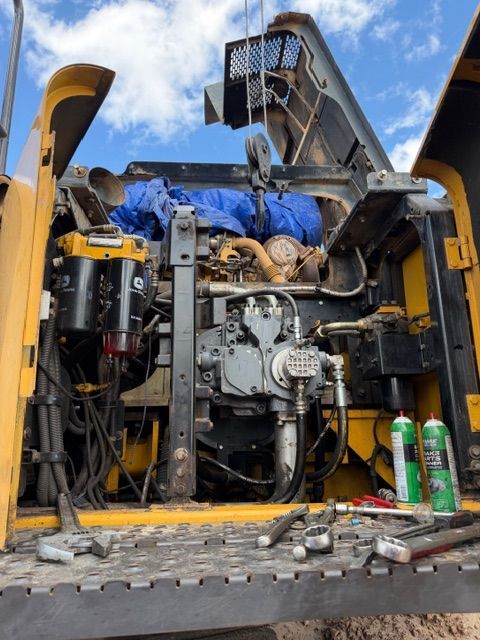 Open service panel of a yellow construction vehicle showing the engine, hydraulic pump, and various tools on the deck.