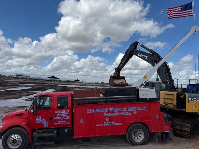A bright red Major Truck Repair service truck parked in a dirt lot next to a large yellow John Deere excavator.