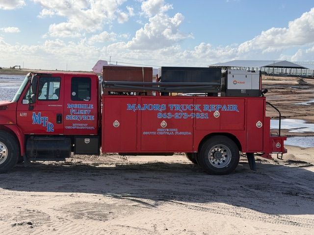 A red Majors Truck Repair service truck parked on a sandy lot under a cloudy blue sky.