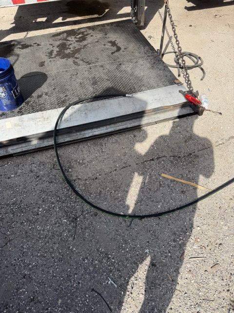 A black power cable lies on concrete near a metal trailer gate, with a blue bucket and a chain visible nearby.