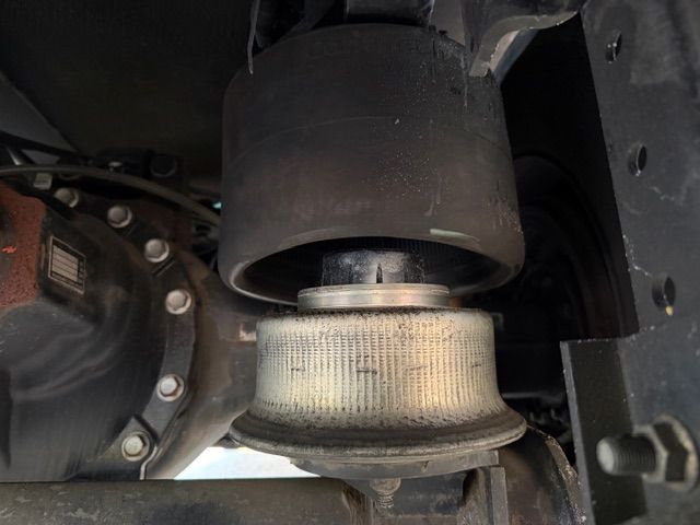 A close-up view of a vehicle's black rubber air suspension bag and metal base mounted above a truck axle.