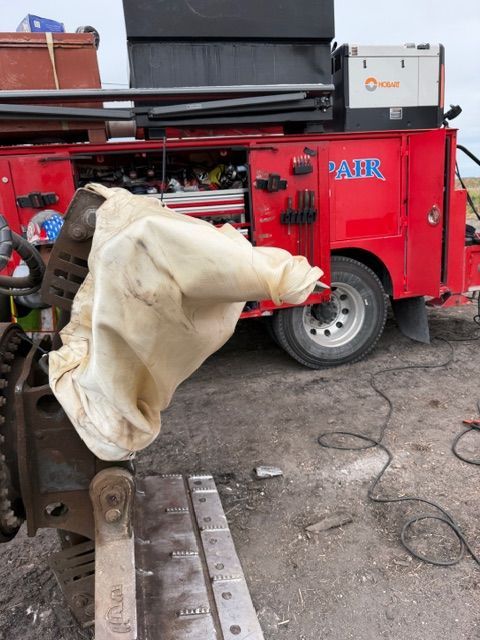 A red service truck parked on a gravel lot next to heavy industrial equipment covered by a white protective cloth.