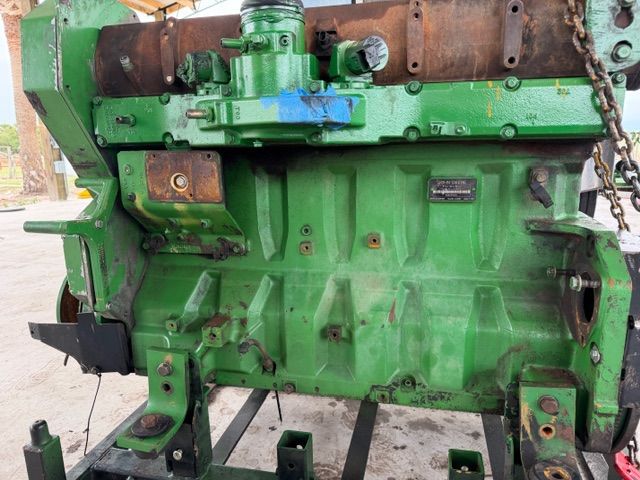 A green, heavy-duty John Deere engine block mounted on a metal frame, viewed from the side in an outdoor setting.