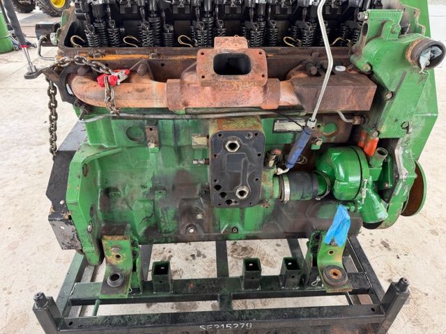A green John Deere diesel engine block with an exposed exhaust manifold, mounted on a metal stand.